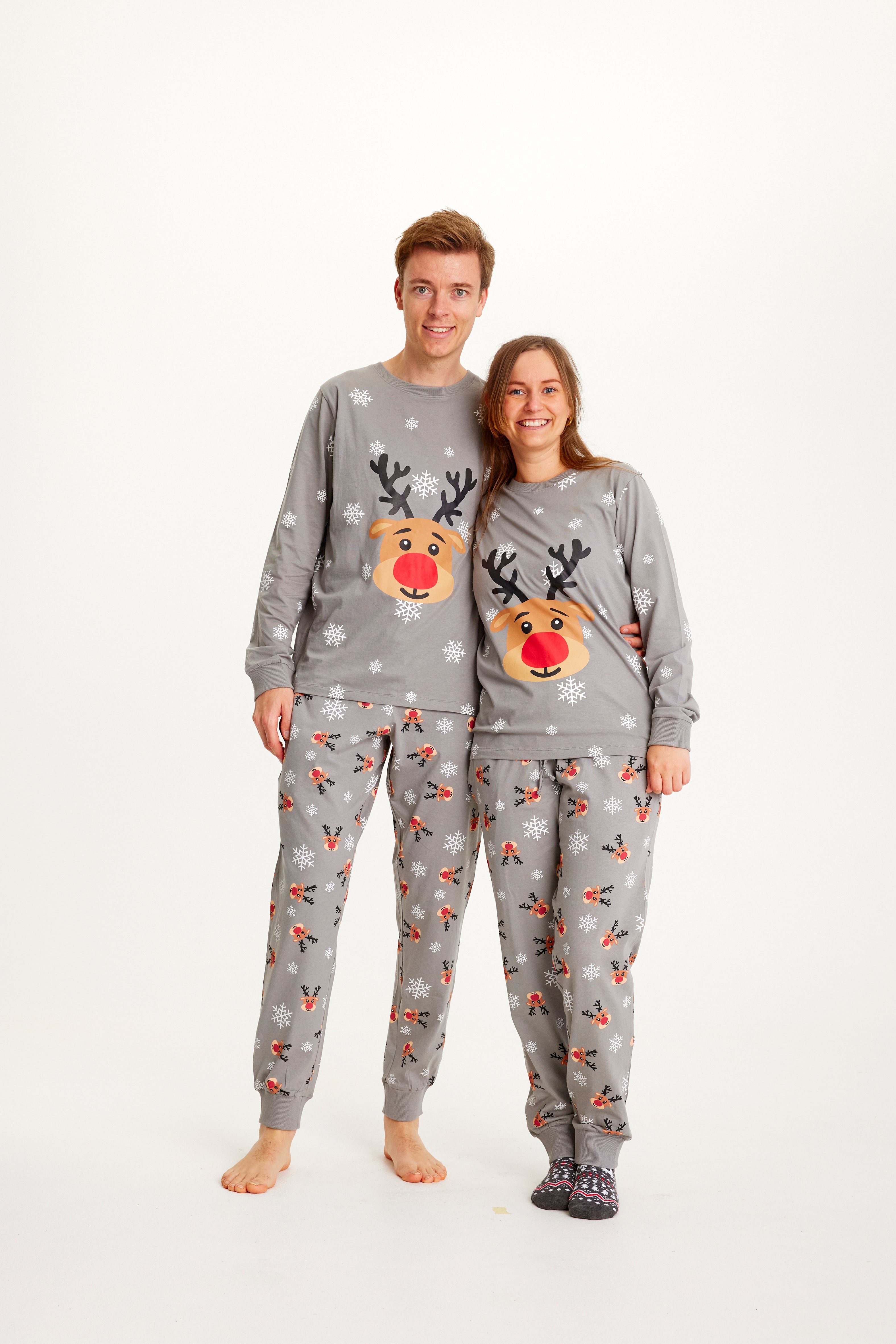 En kvinne og en mann i grå julepyjamas med reinsdyr og snøfnugg.